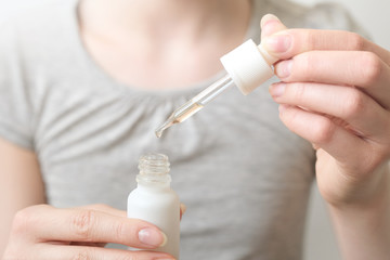 Female hand holds a pipette with a medical solution over a white bottle. Drops for nose, eyes or cosmetic oil. Copy space, mockup