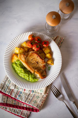 Succulent pork steak fillet with mushy peas, roast potatoes and tomatoes. Overhead vertical image