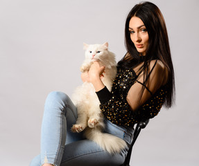 Portrait of caucasian brunette girl model on a white background in studio. Model is sitting on a chair with a white cat in her arms.