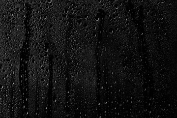 Drops of water flow down the surface of the clear glass on a black background.	
