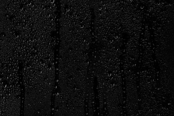 Drops of water flow down the surface of the clear glass on a black background.	