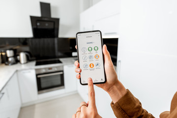 Woman controlling kitchen appliances with a smart phone, close-up on mobile device with launched smart home application. Smart home concept