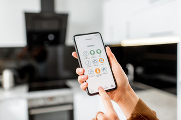 Woman controlling kitchen appliances with a smart phone, close-up on mobile device with launched smart home application. Smart home concept