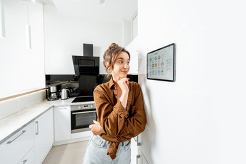 Young woman controlling kitchen appliances with a digital tablet on the wall with launched smart home application. Smart home concept