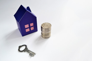 Paper house, key and money coins on a white background