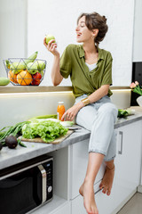 Full length portrait of a young and cheerful woman with healthy raw food on the kitchen at home....