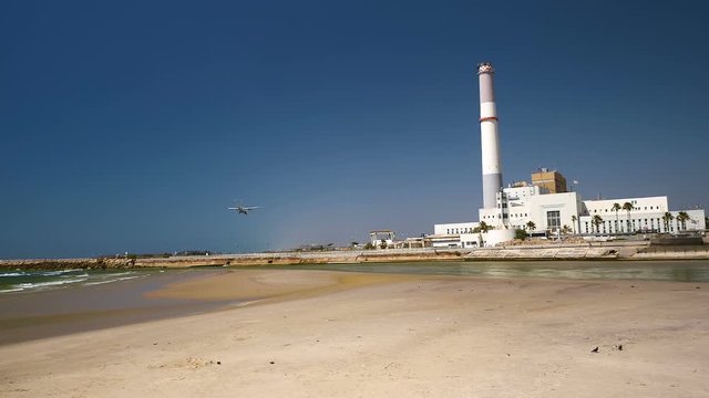 Passenger airplane landing in Sde Dov airport in Tel Aviv. View from the beach near the Reading power plant. Dolly shot.