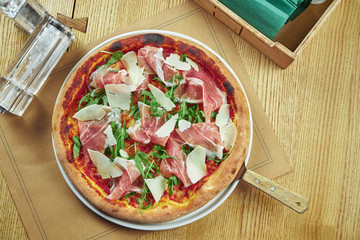 Appetizing baked pizza with prosciutto di parma, parmesan and arugula with crispy crust on a wooden...