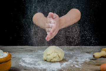 Man hands kneading bread dough on a wooden table with black background