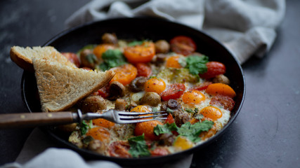 the process of preparing a family breakfast of fried eggs with tomatoes, mushrooms and herbs on a dark table