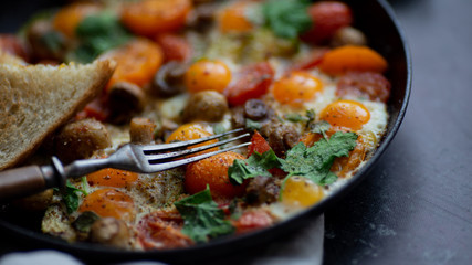 the process of preparing a family breakfast of fried eggs with tomatoes, mushrooms and herbs on a dark table
