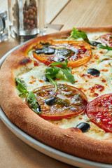 Appetizing baked pizza with melted cheese and different types of tomatoes with a crispy crust on a wooden background. Restaurant serving. Pizza Margherita
