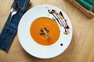 Fresh, veggie pumpkin cream soup with cream in a white plate on a wooden background. Restaurant...