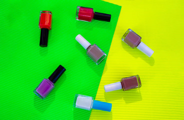 Bright colorful nail polishes bottles on green and yellow paper background.