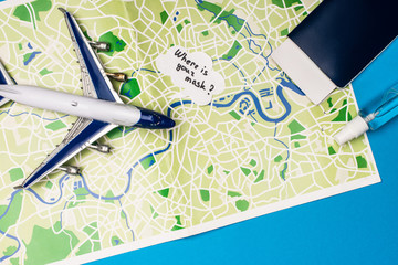 Top view of toy plane near speech bubble with where is your mask lettering near passport and bottle of hand sanitizer on map on blue surface