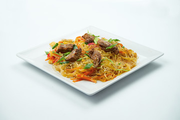 Tasty udon noodles in sweet and sour sauce with vegetables and beef in a white plate on a gray background. Close up view