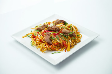 Tasty udon noodles in sweet and sour sauce with vegetables and beef white plate on a gray background. Top view with copy space