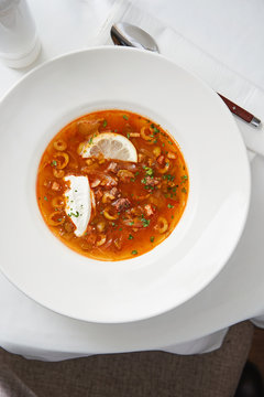 Plate of hot solyanka soup with olives and beef served with sour cream and chopped parsley