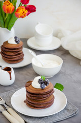 Stack of chocolate pancakes on a white plate with chocolate sauce, whipped cream, blueberries and blackberries on top of a concrete background. Delicious breakfast. Vertical orientation. Copy space.
