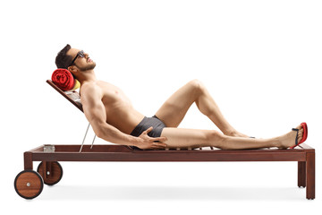 Fit young man lying on a wooden sunbed in swimwear