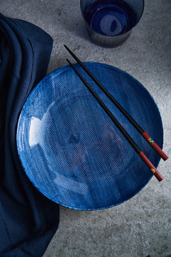 Blue plate on cement surface with linen napkin and sticks..