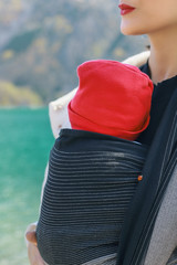 Beautiful young mother with her infant baby in sling outdoor. Mother is carrying her child and...