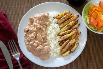 beef stroganoff with rice and french fries on white plate 
