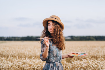 Portrait of smiling female artist with curly hair in hat. Girl draws a picture of a landscape in a...