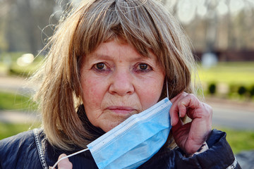 portrait of elderly woman putting medical mask on her face outdoors.