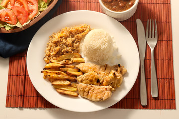 Dish of grilled chicken fillet with rice, beans, french fries and farofa on white plate. Top view.