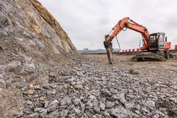 Hydraulic breaker during road construction on rocky soil. Heavy machinery in earthmoving...