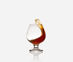 Glass glass with an alcoholic drink or cognac and splashes on a light background. Isolated, splash.
