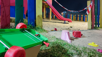 Empty Playground, quarantine. Scattered toys on the ground next to the closed Playground at night. Prohibiting tape.