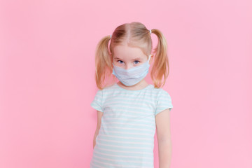 Little blonde girl with two ponytales in a medical mask face on a pink background looking at the camera