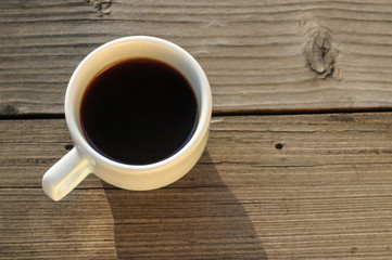Black coffee in a white cup on a wooden background. White cup with black coffee on the balcony in the rays of the evening sun.