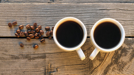 Black coffee in a white cups near the coffee beans on a wooden background.