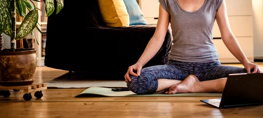 Fototapeten Frau macht Yoga-Training zu Hause und schaut sich Videos online auf dem Laptop an © Melinda Nagy