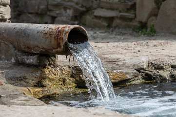 rusty pipe with flowing water into the river. spring with clear spring water. drainage system or...