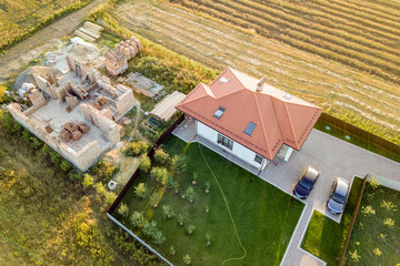 Top down aerial view of two private houses, one under construction with concrete foundament and brick walls and another finished with red tiled roof.