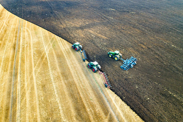 Obraz premium Aerial view of a tractor plowing black agriculture farm field after harvesting in late autumn.