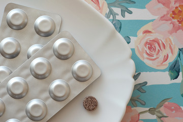 Iron pills on a plate. Many tablets of Ferrous sulfate. Supplement use for Iron Deficiency Anemia. Floral retro background. Pastel color.