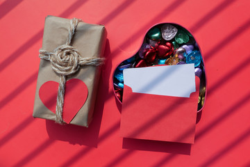 close up of candy in a heart shape box and envelope on red background 