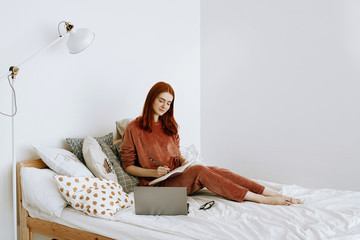 The concept of distance education or working from home in quarantine. A young red-haired woman in...