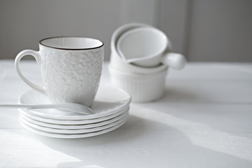 white tea cup, plates and saucer on a shelf. minimal style tableware. trendy uncluttered kitchen. elegant modern monochrome design.