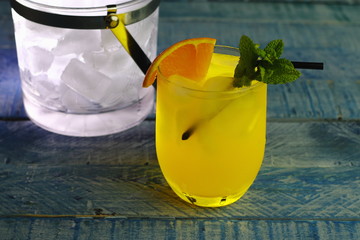 cóctel de naranja refrescante con mucho hielo, naranja y menta sobre un fondo azul
