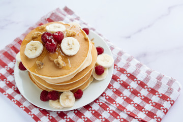breakfast, pancakes with raspberry, nuts, banana and honey on a white plate