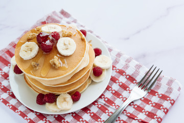 breakfast, pancakes with raspberry, nuts, banana and honey on a white plate