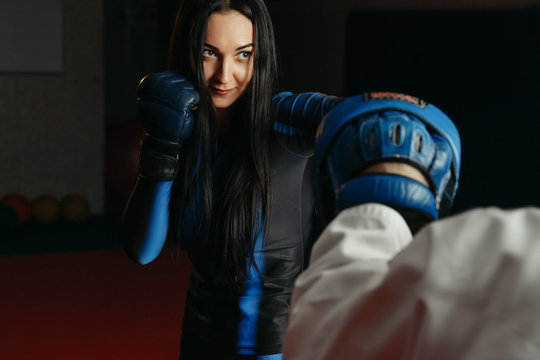 White woman is engaged with the trainer in self-defense lesson, studio, dark background. Concept of sport and boxing