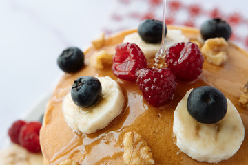 breakfast, pancakes with raspberry, blueberry, nuts, banana and honey on a white plate