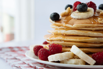 breakfast, pancakes with raspberry, blueberry, nuts, banana and honey on a white plate